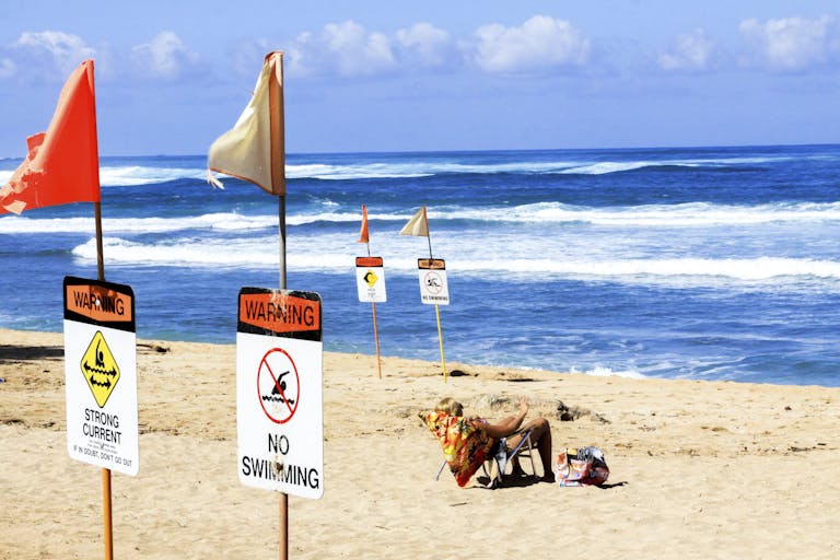 Sunny beach scene with no swimming warning signs, ocean waves, and a person relaxing.