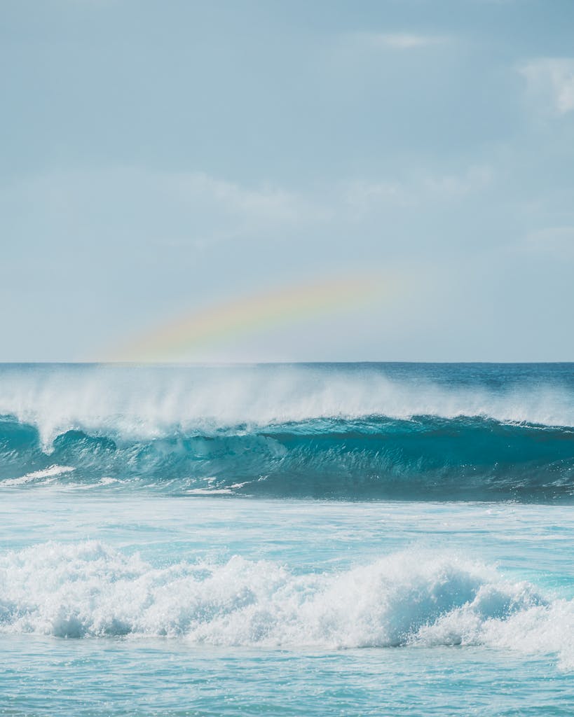 Beautiful ocean waves crashing under a vivid rainbow on the horizon in a tranquil seascape.