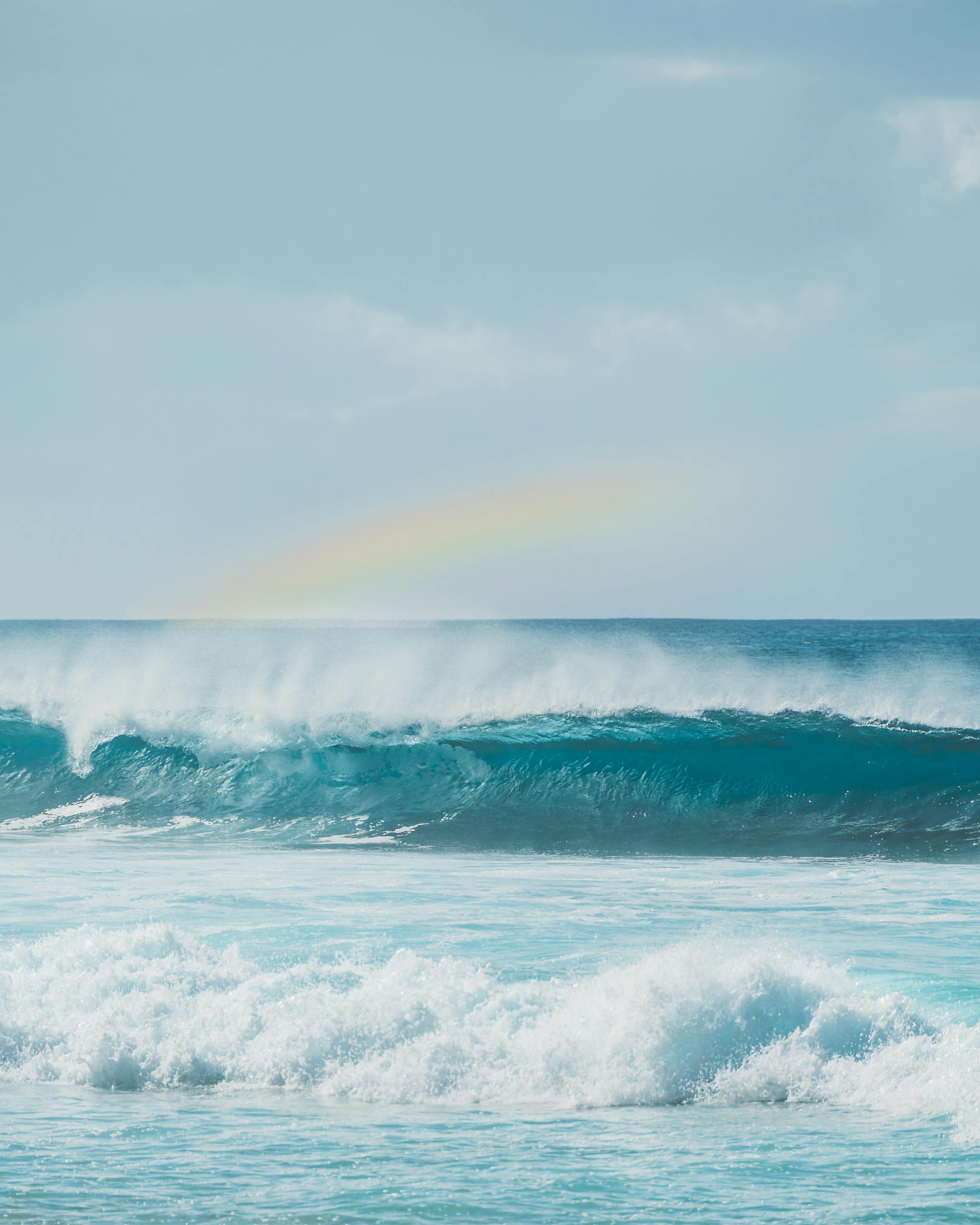 Beautiful ocean waves crashing under a vivid rainbow on the horizon in a tranquil seascape.