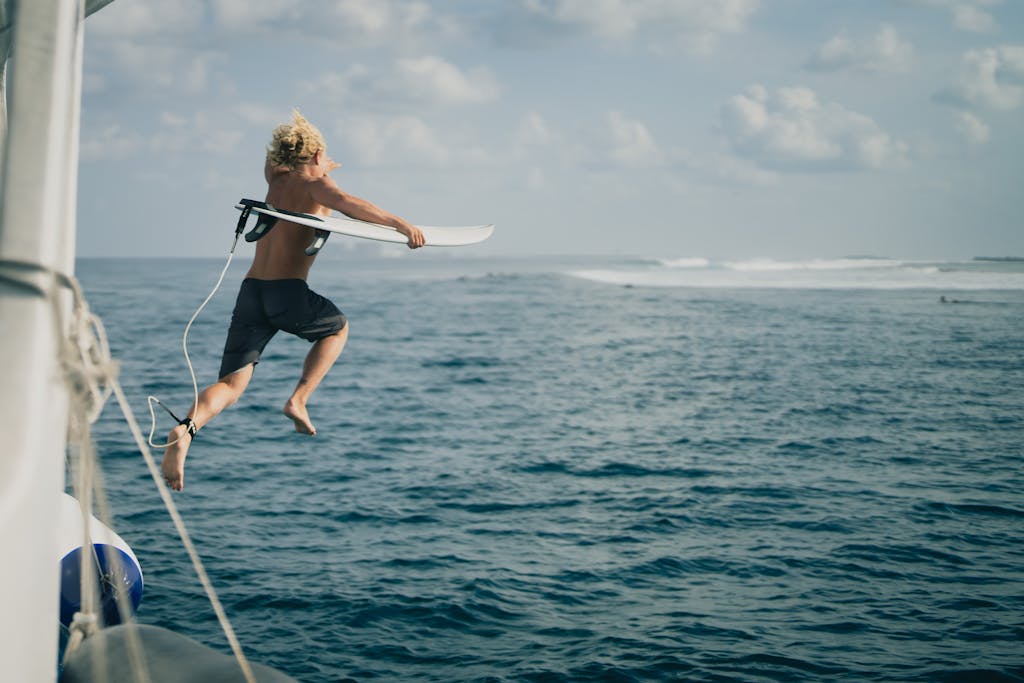 An energetic man jumps from a boat into the sea with his surfboard, embracing adventure.