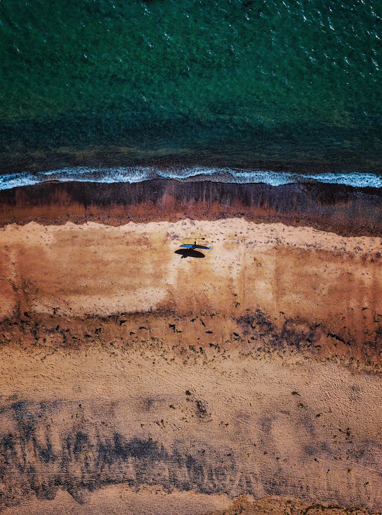 Stunning aerial photograph of Exmouth Beach showing waves and a lone SUP surfer on the sand.