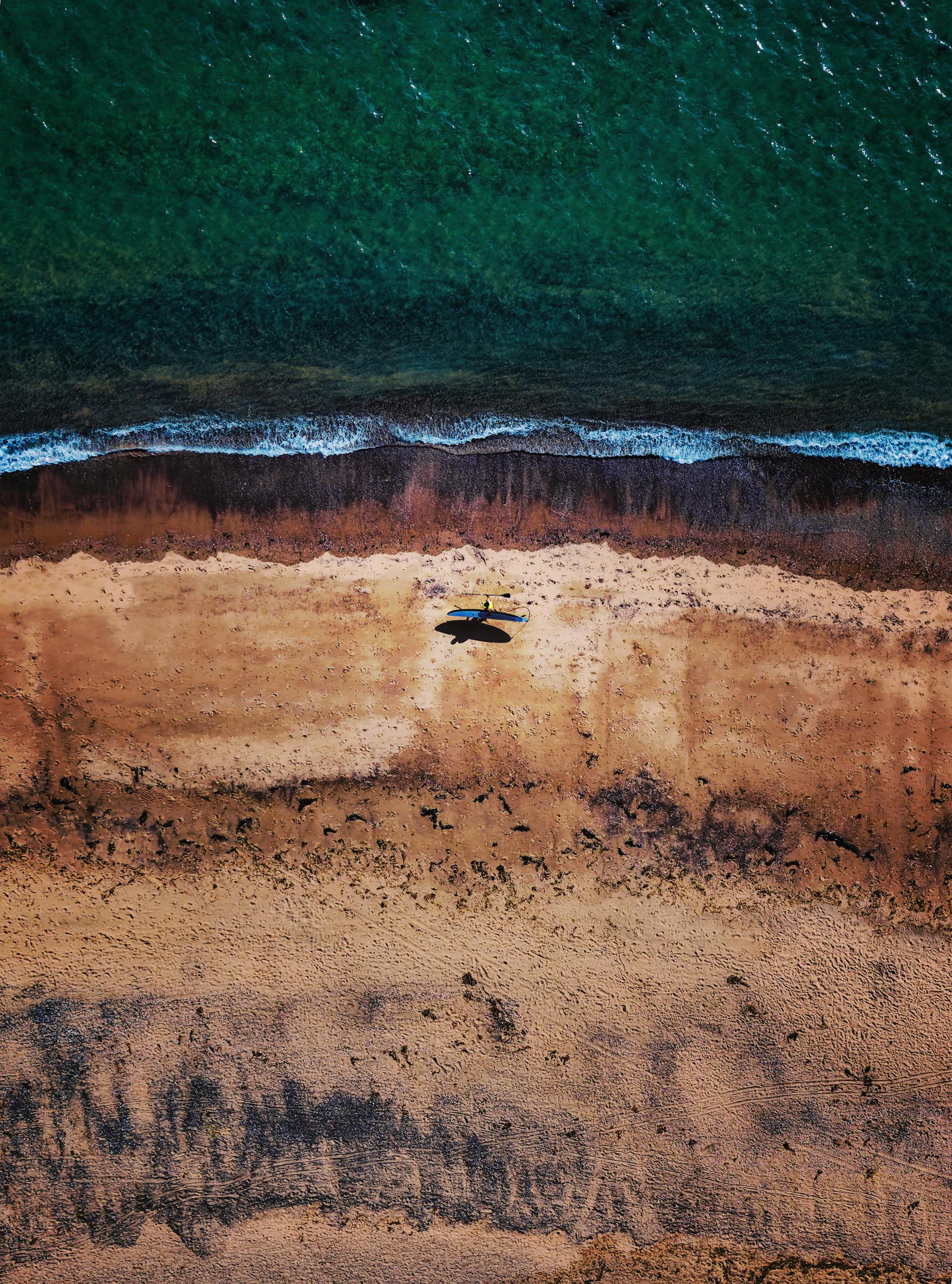 Stunning aerial photograph of Exmouth Beach showing waves and a lone SUP surfer on the sand.